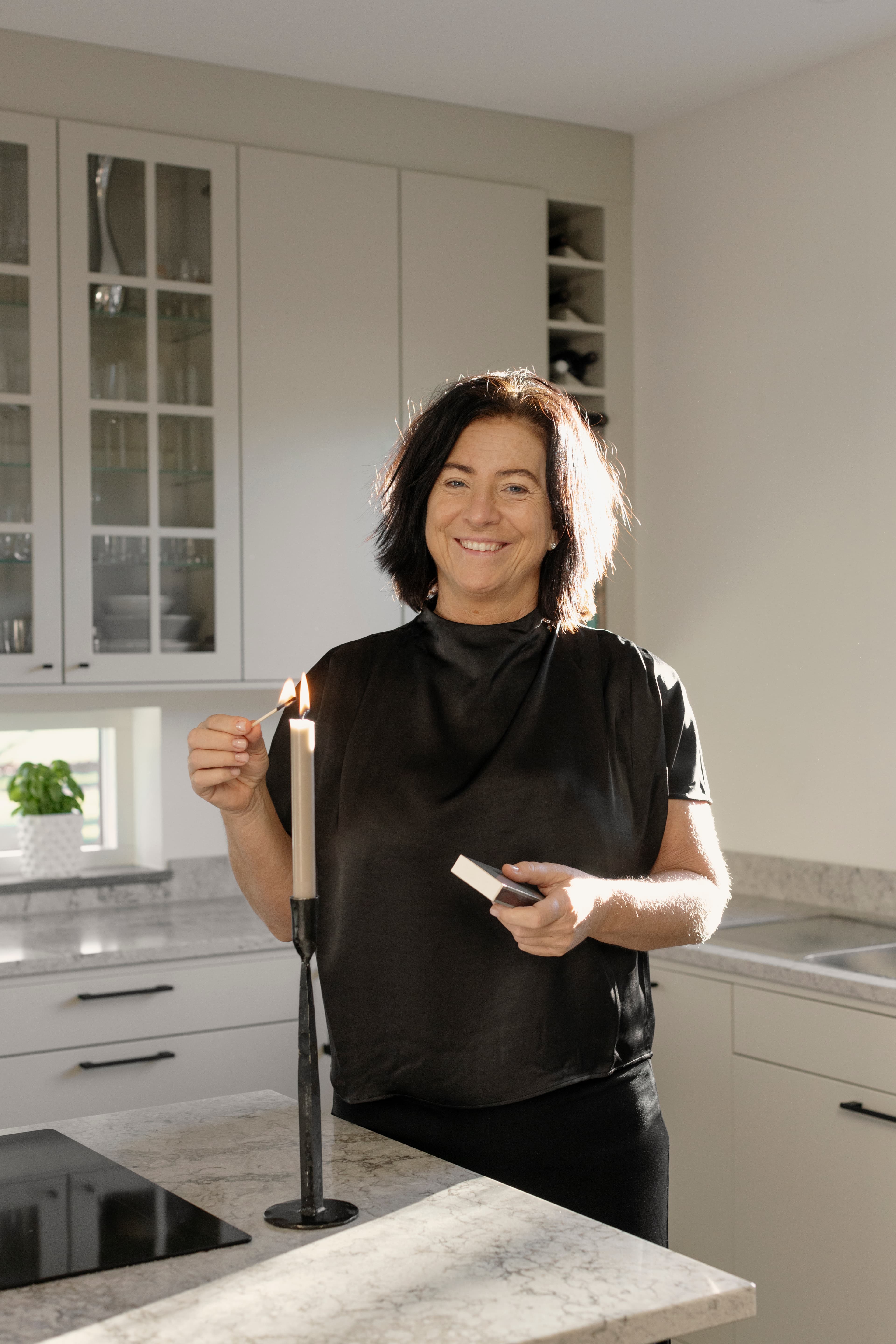 Kvinna som tänder ljus vid köksö.