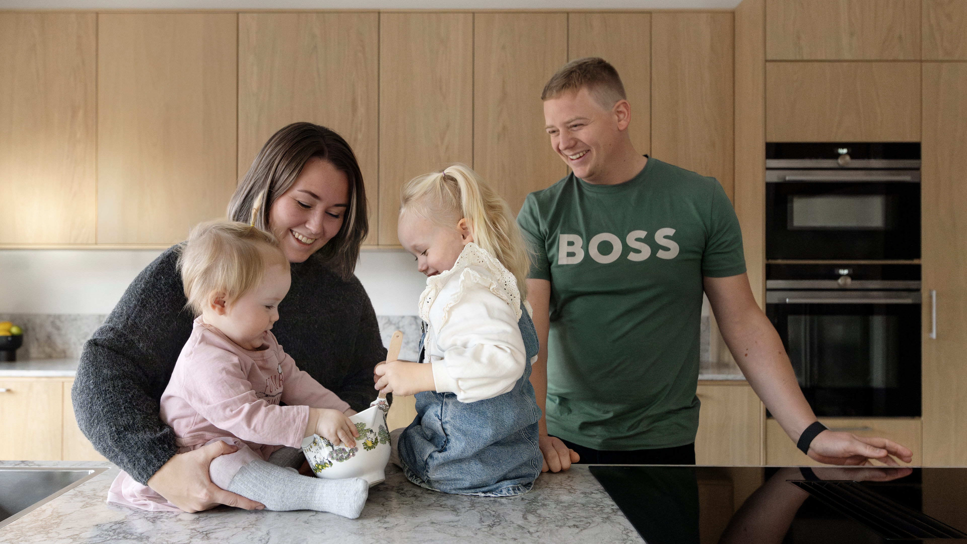 Familj står i ett kök. Två barn sitter på köksön.