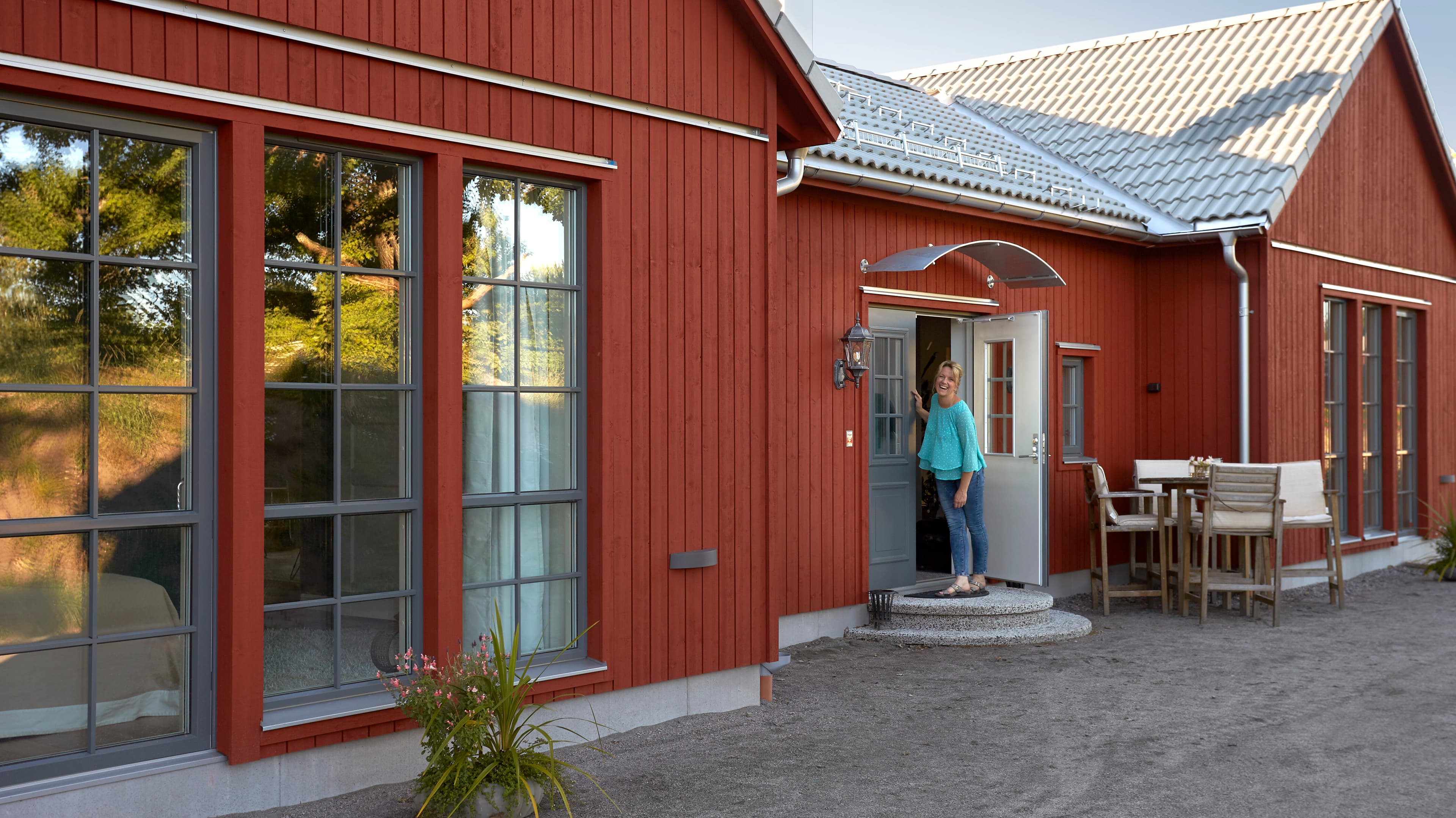 Kvinna med blå blus står vid ingången till ett rött hus. 