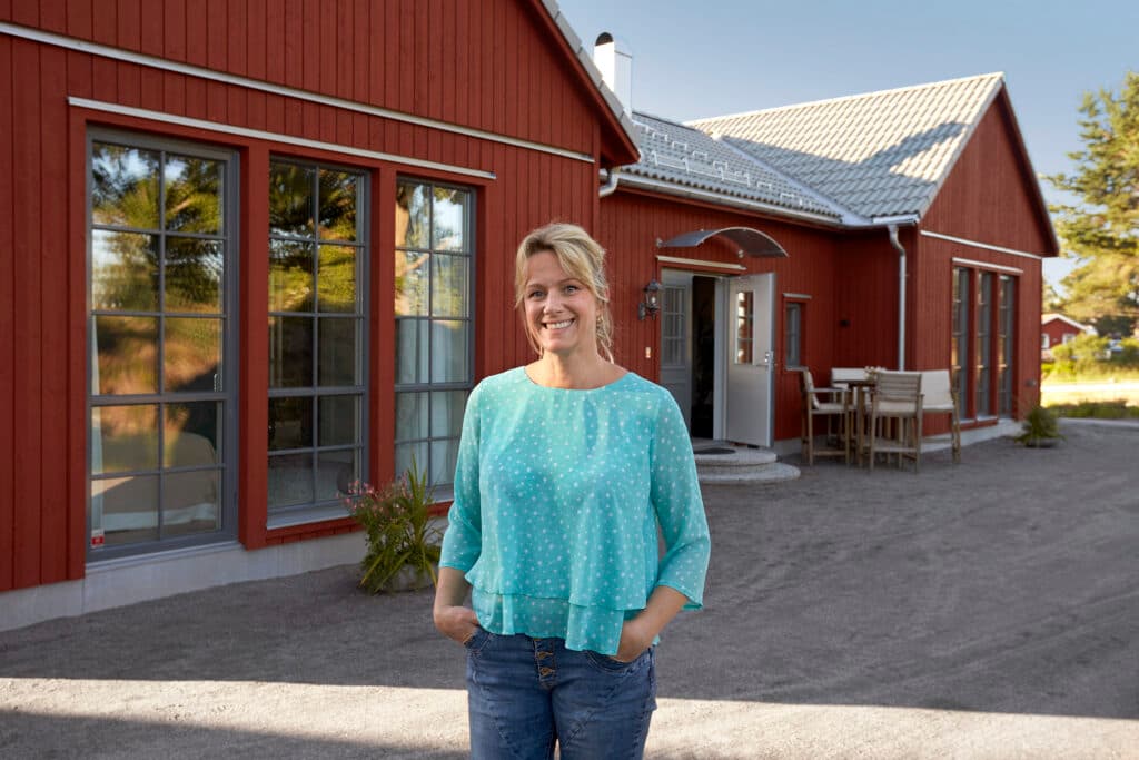 Kvinna med blå blus står framför ett fött hus. 