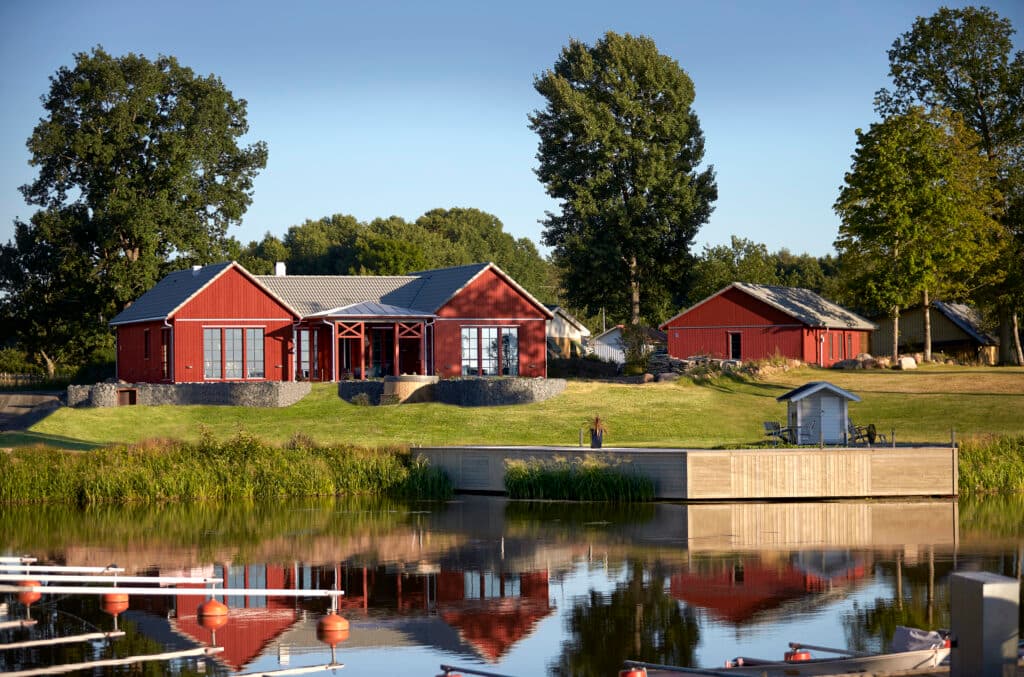 Bild på ett rött hus med gräs och en sjö framför.