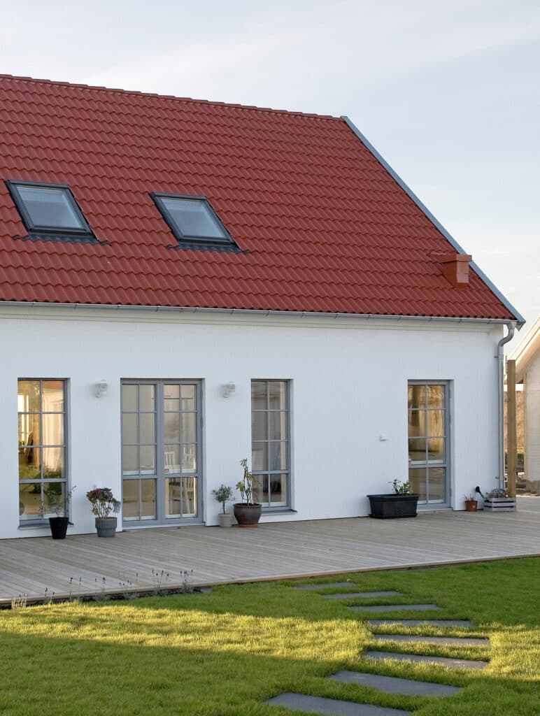 Bild på ett hus med vit puts och rött tak. 